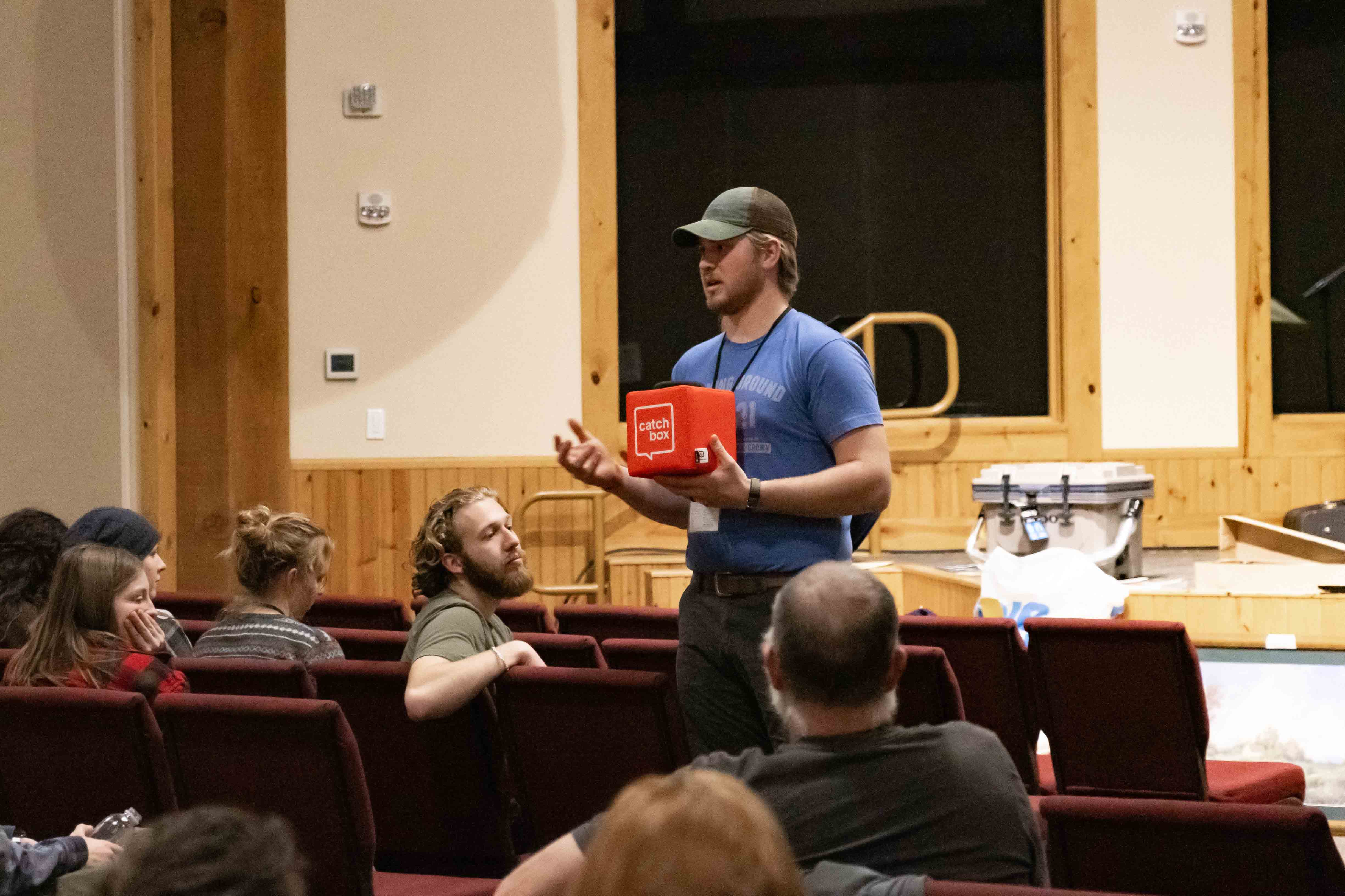 Man holding a red Catchbox Cube microphone while engaging attendees seated in a church