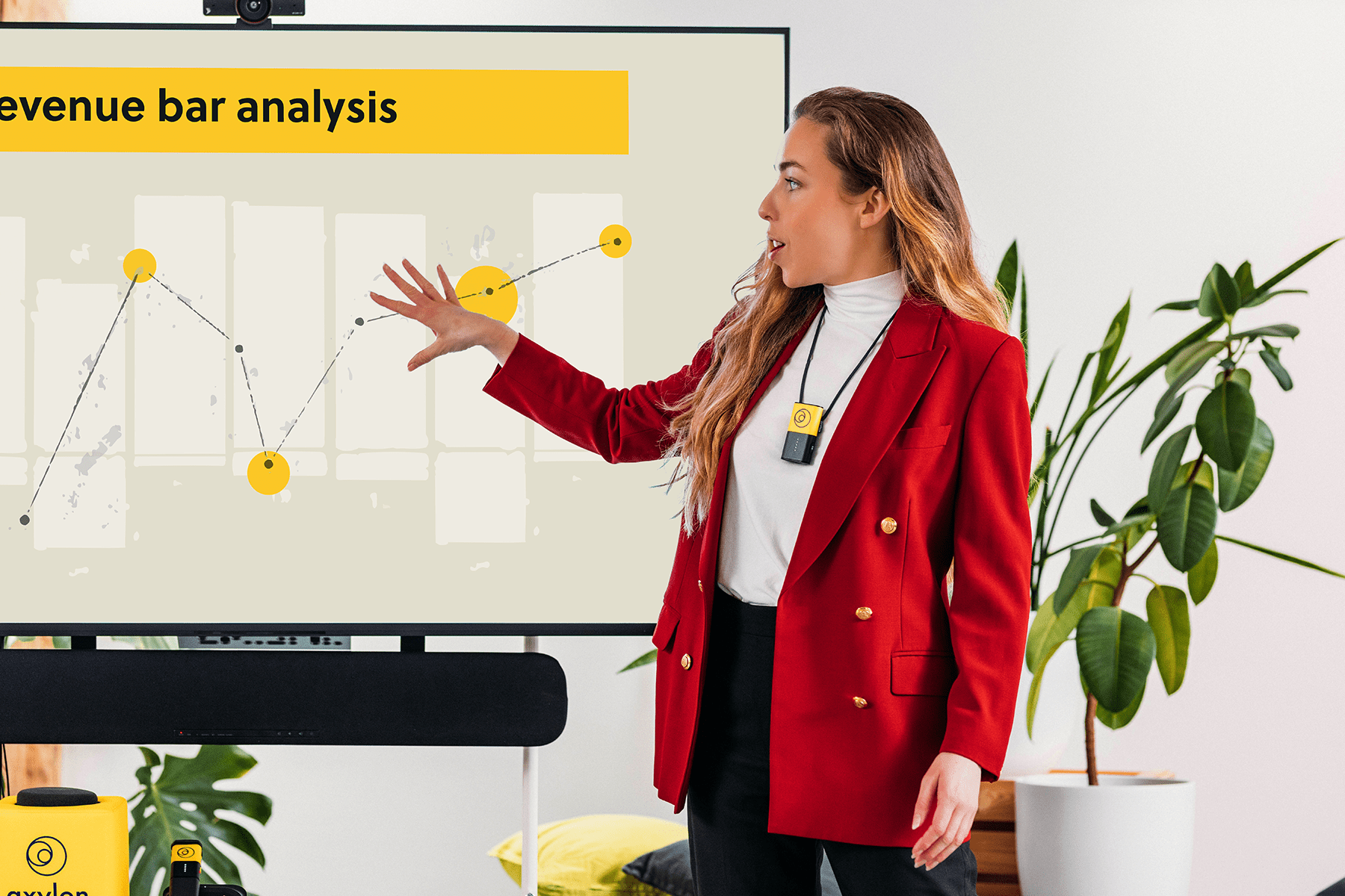 A person presenting an analysis, standing next to a screen, and amplifying their voice using a Catchbox Clip presenter microphone.