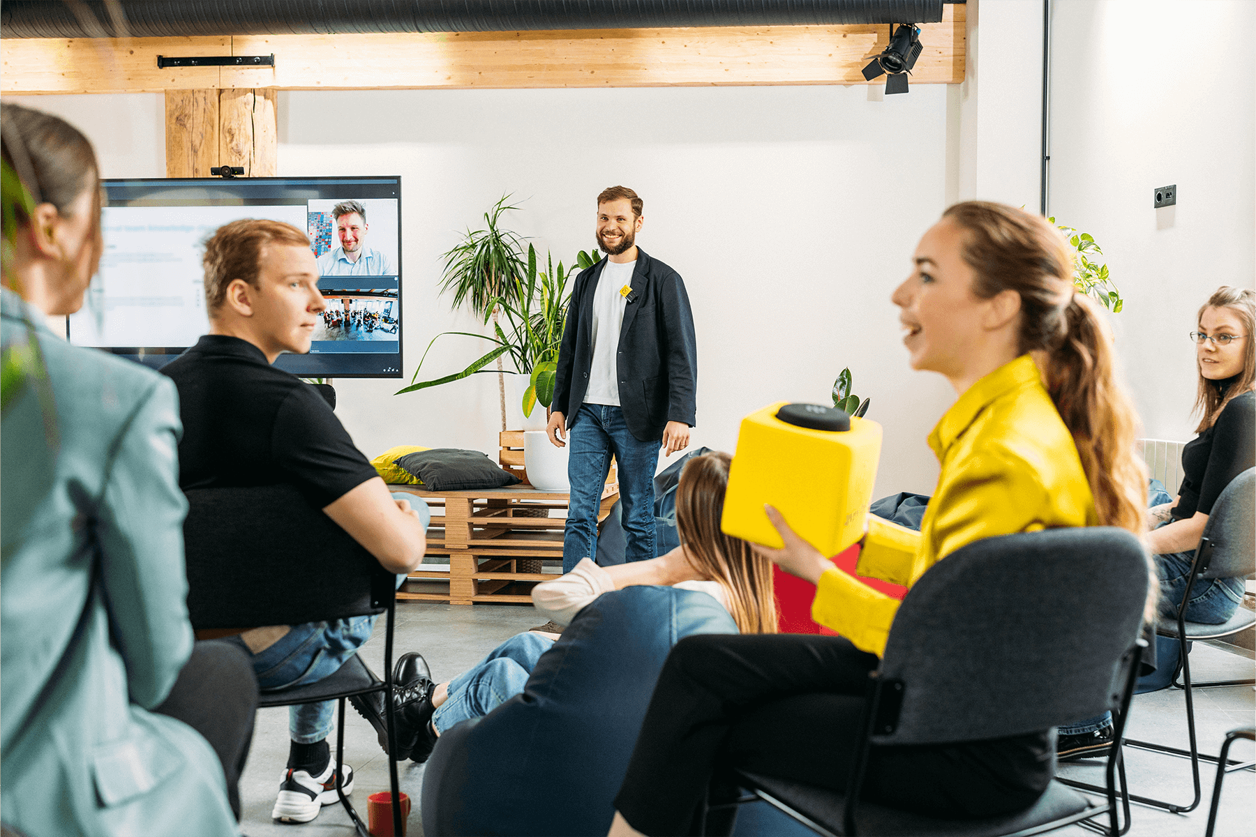 A professional woman engages with an office presentation while holding a customized Catchbox Cube audience microphone. The meeting leader, wearing a Catchbox Clip, listens attentively to the audience.