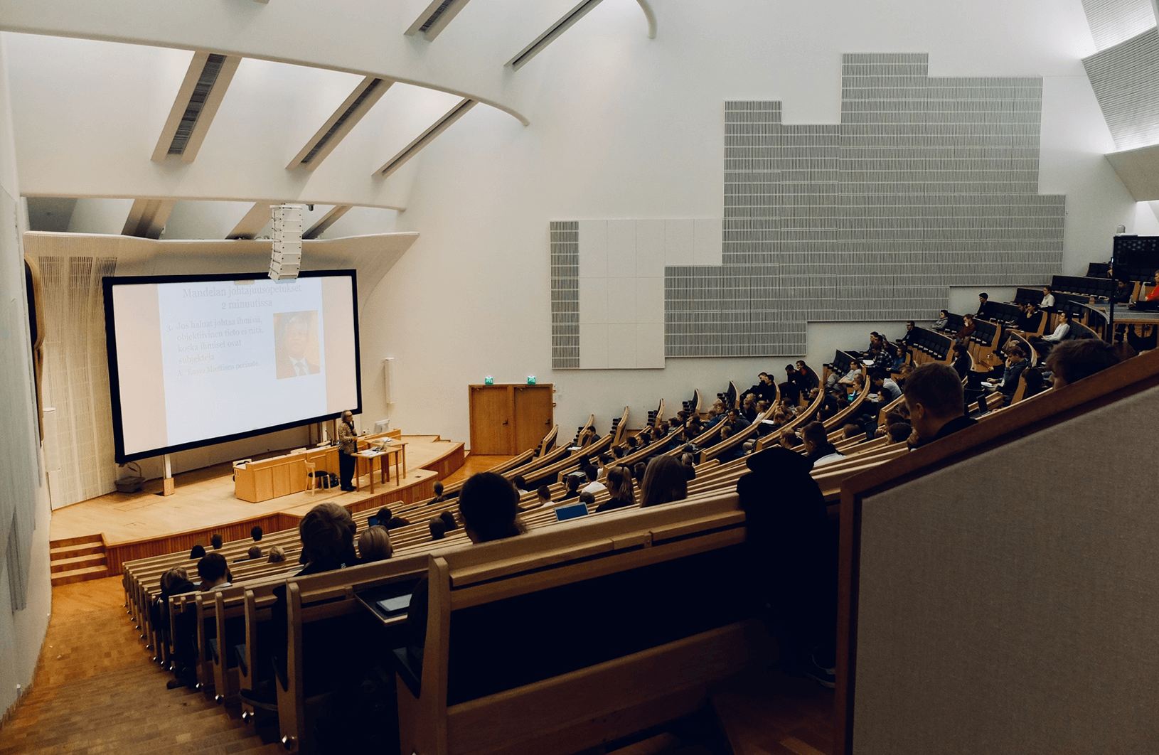 Accessibility in higher education: Large university auditorium with diverse students attending a lecture. Rows of seating, a podium, and students focused on the speaker.